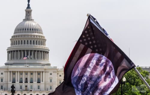 The American flag with a small circle of a shadow in front of the Paris building outside in an overcast sky.