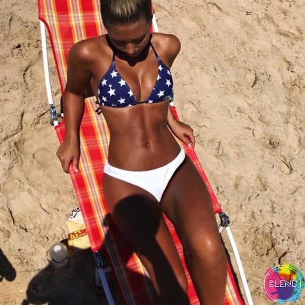 Tan lady who had negative body image lays on red gingham beach chair navy and white star bikini top and white bikini bottoms looking down at the sand.