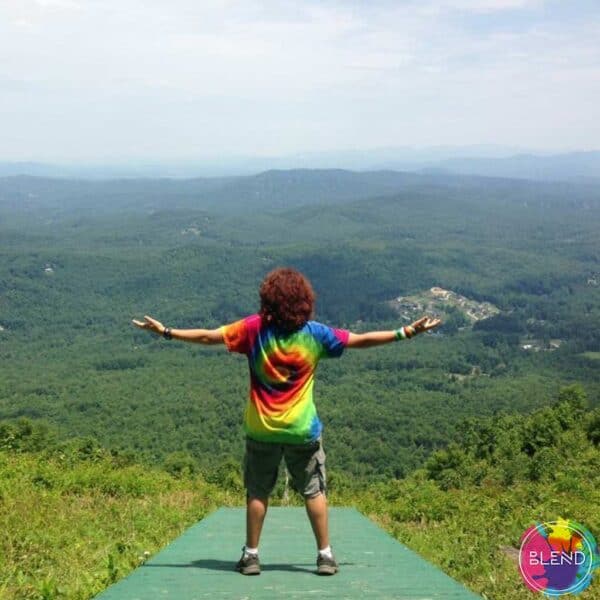 The author wearing a tye dye shirt and cargo shorts while looking at a view from a mountain top.