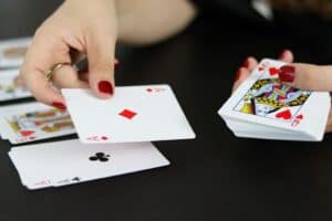 poker-4515980_960_720 An elder lady with a ring on her finger places her hand on the red Ace card, and her other hand is on a big stack of cards.