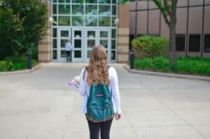 college-anxiety-stress A young brunette girl, wearing a grey sweater and a blue backpack, and jeans, walking to her university.