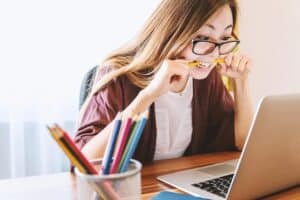 cover Woman in a dark cardigan and white shirt, looking at the computer, biting her pencil