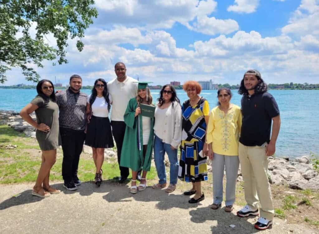 Large extended family poses outdoors by a river, celebrating a graduation.