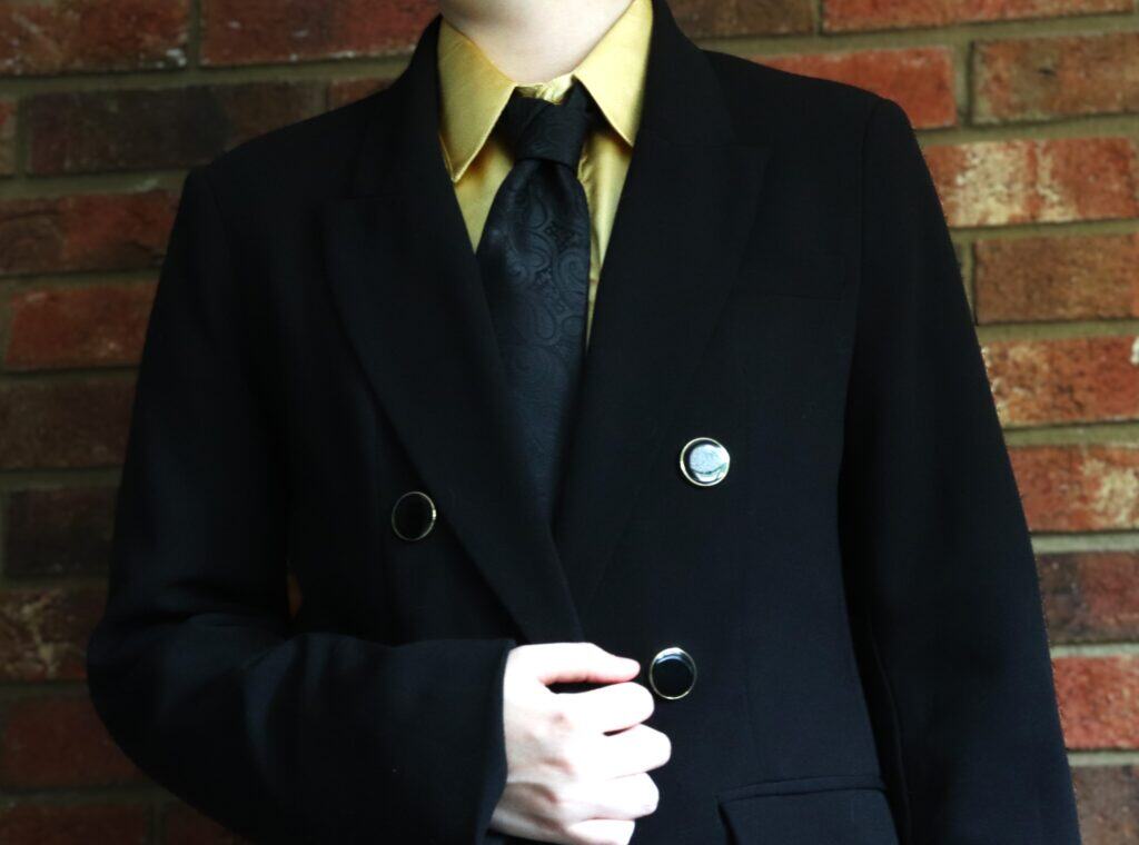 A man in a suit and tie stands confidently against a textured brick wall.