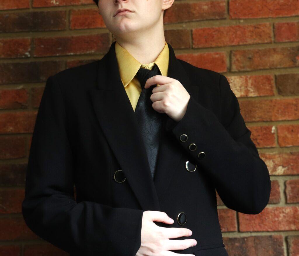 A man dressed in a black suit stands confidently, showcasing a formal and professional appearance.