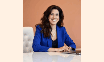 A woman wearing a blue jacket is seated at a table, engaged in conversation or contemplation.