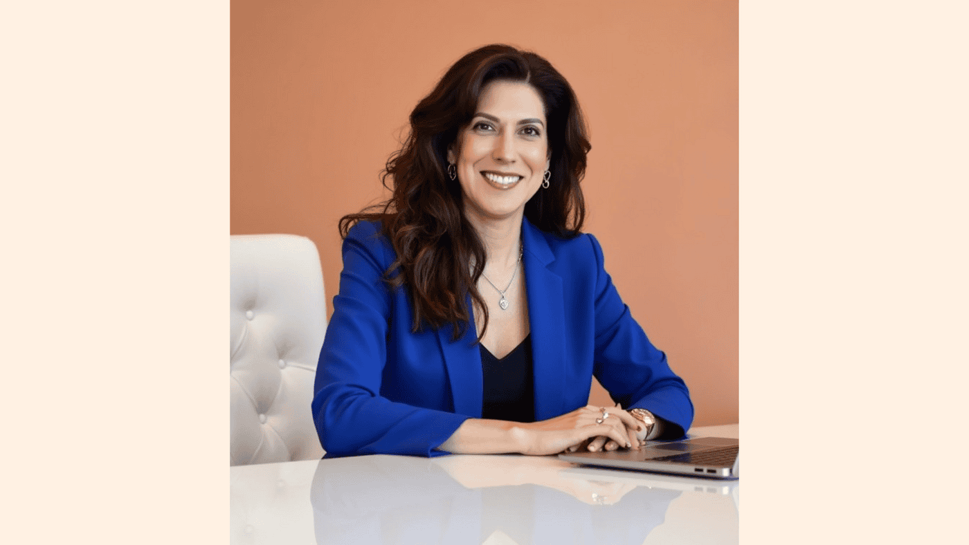 A woman wearing a blue jacket is seated at a table, engaged in conversation or contemplation.